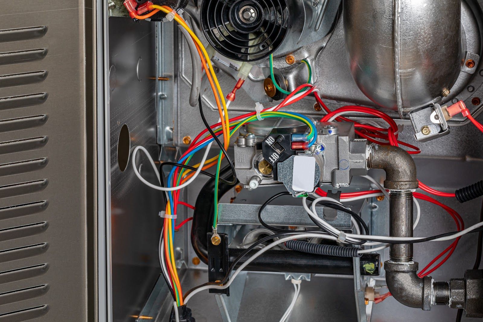Inside of a furnace, showing wiring, gas valve, and blower fan.