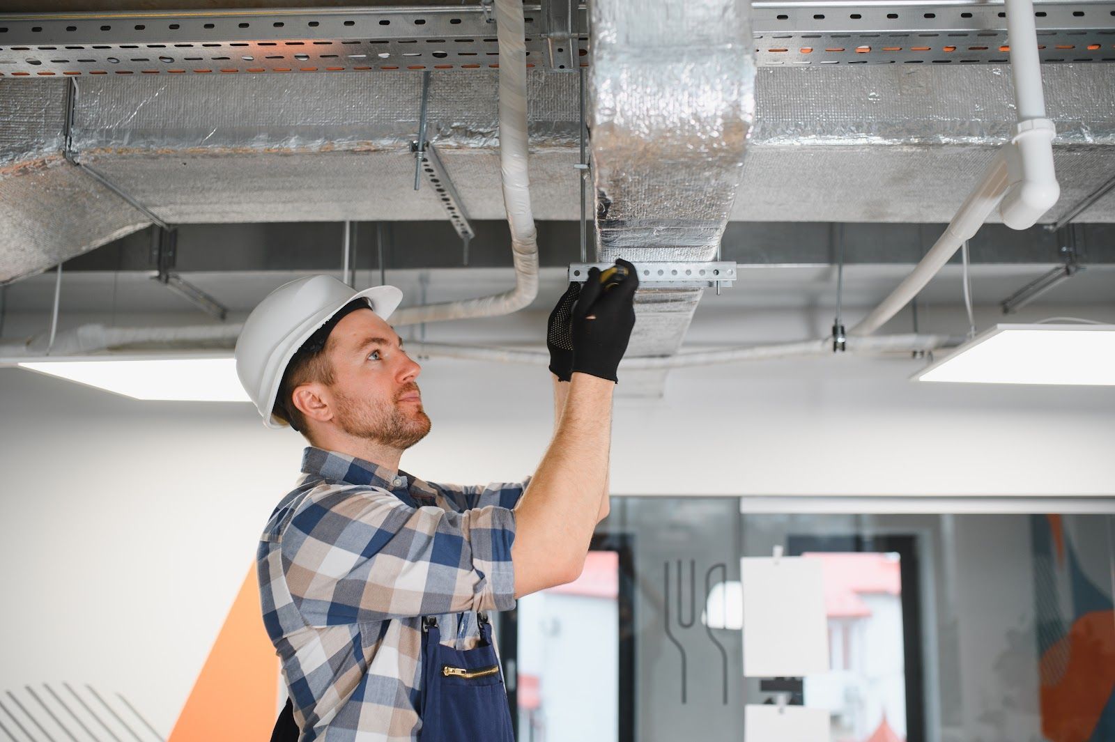 Man in hard hat working on ductwork in a commercial building.