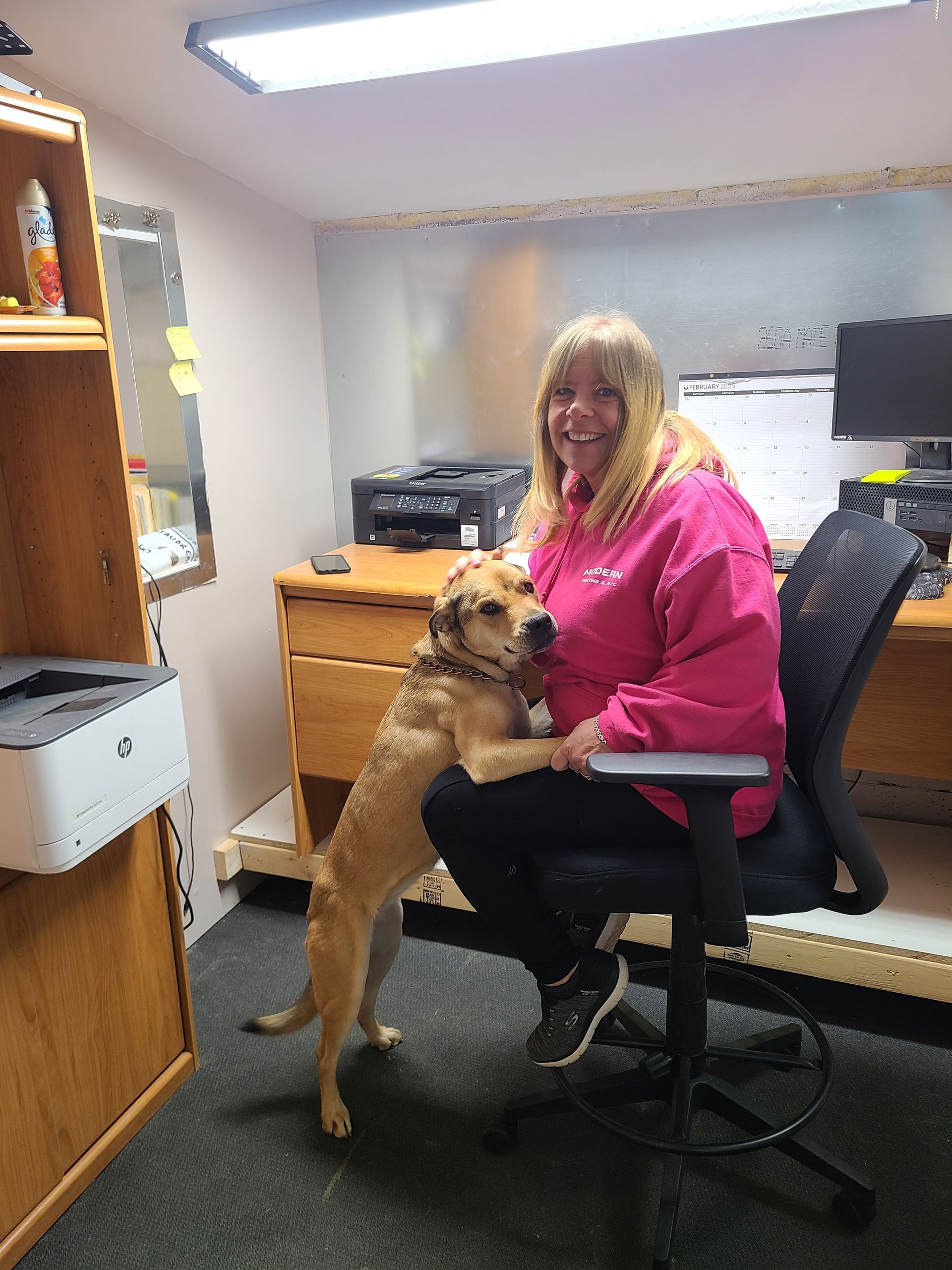 A woman is sitting at a desk with a dog on her lap.