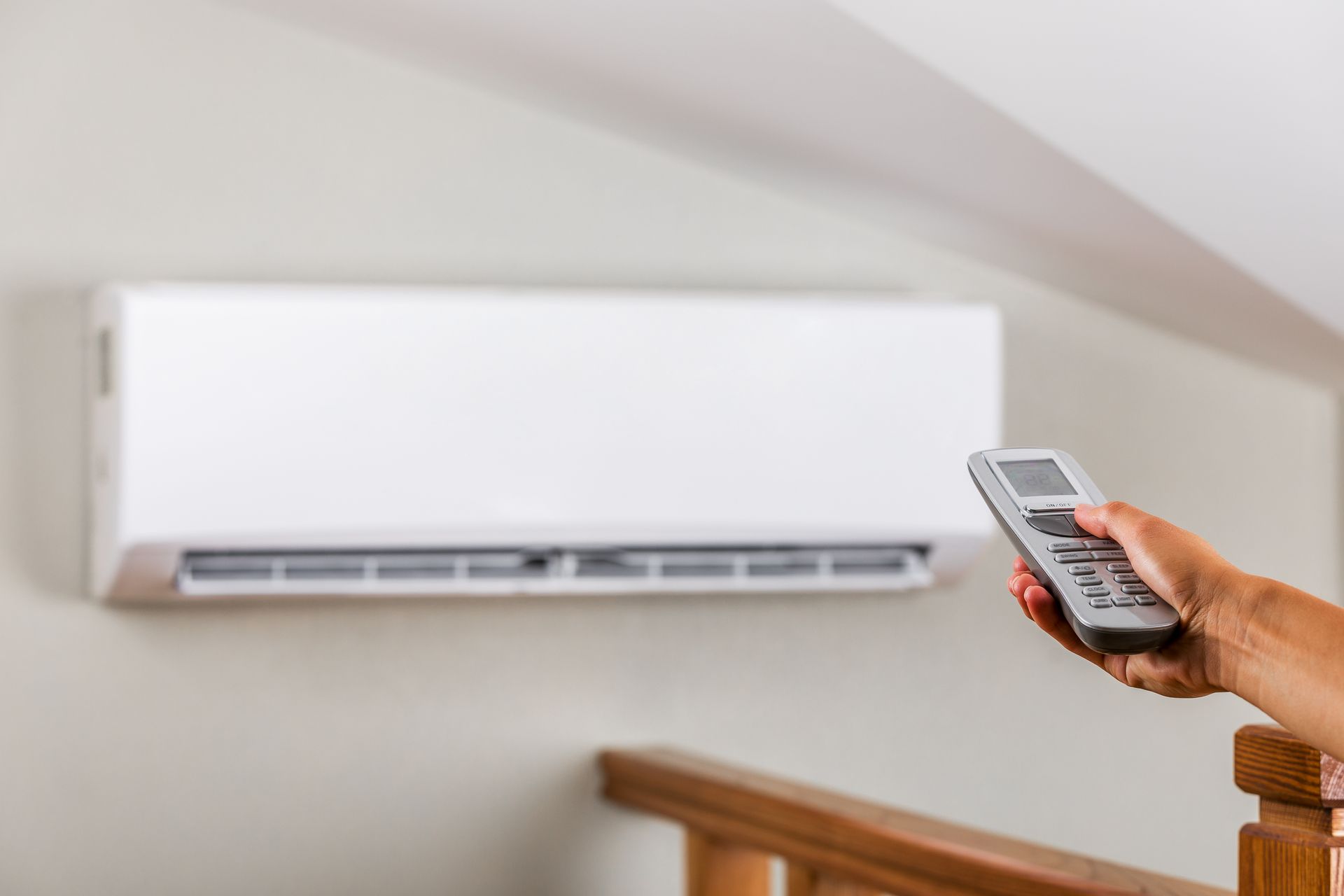 Hand holding remote, aiming it at a white wall-mounted air conditioner.