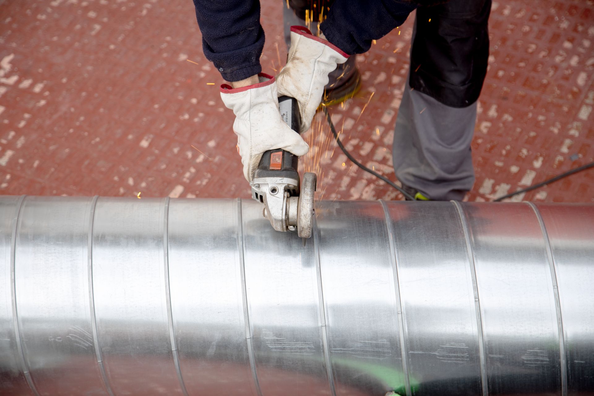 A man is grinding a metal pipe with a grinder.
