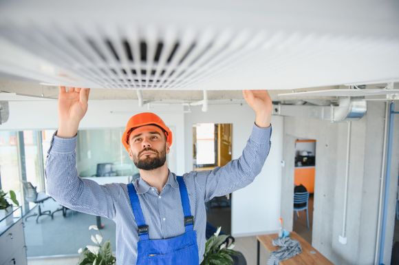 A man wearing a hard hat and overalls is working on a ceiling.