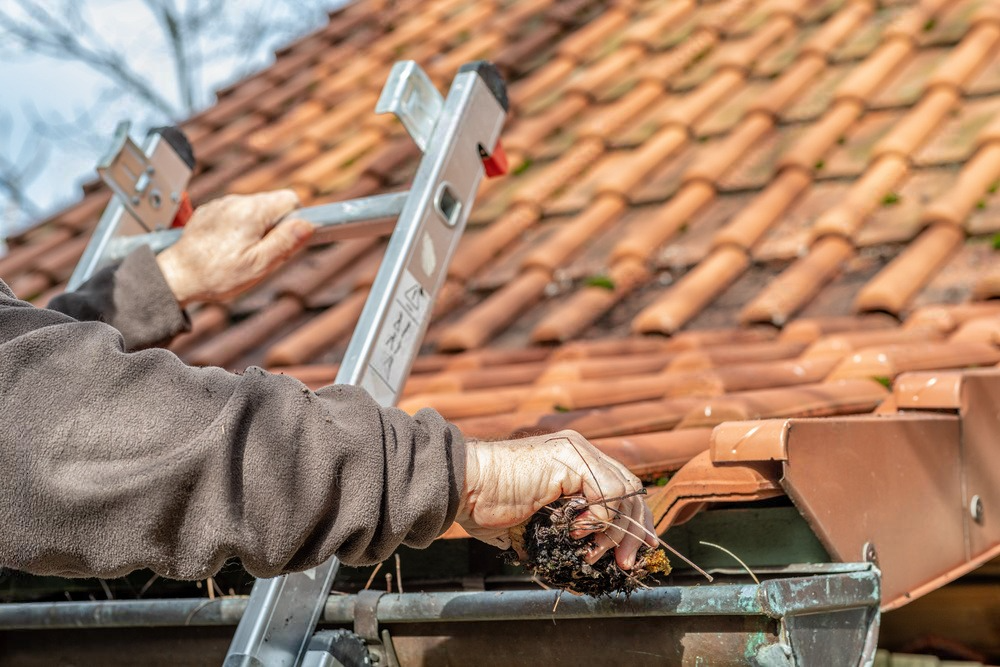 a man is using a ladder to clean a gutter on a tiled roof .