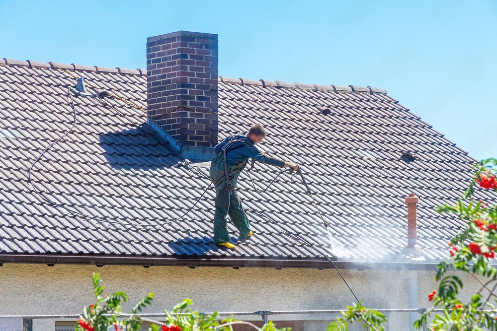a man is cleaning the roof of a house with a high pressure washer .