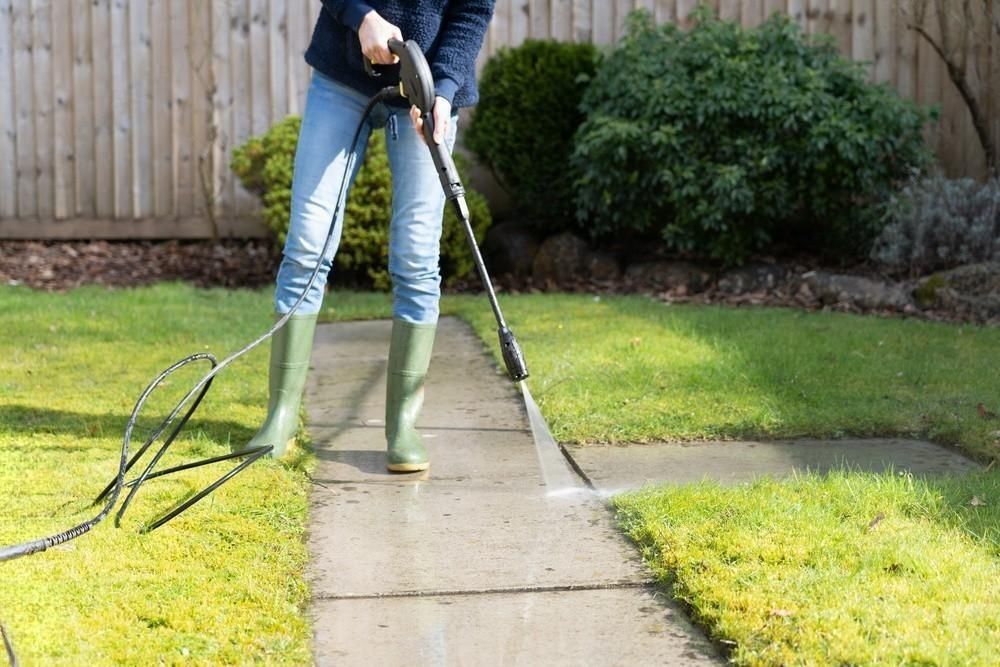 a woman is using a high pressure washer to clean a sidewalk .