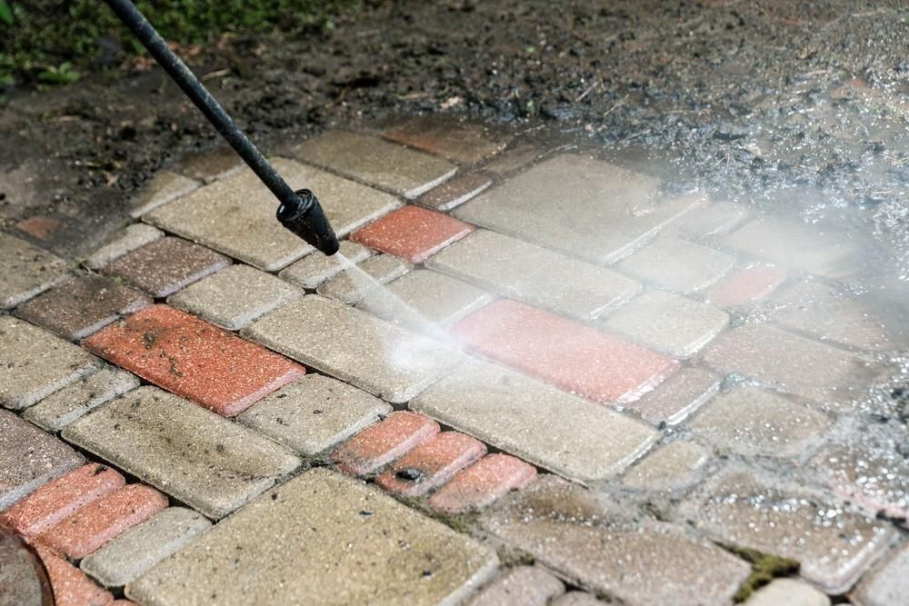 a person is using a high pressure washer to clean a brick walkway .
