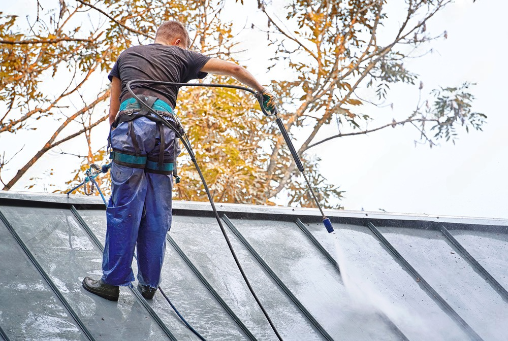 a man is cleaning the roof of a building with a high pressure washer .