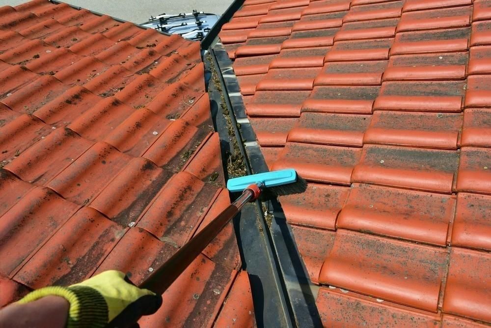 a person is cleaning a gutter on a tiled roof .