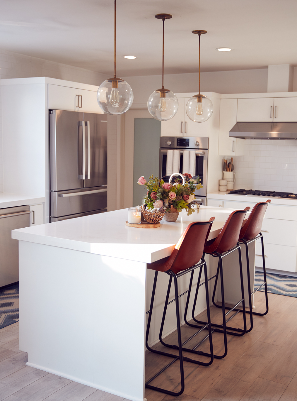 A kitchen with white cabinets , stainless steel appliances and a large island with stools.