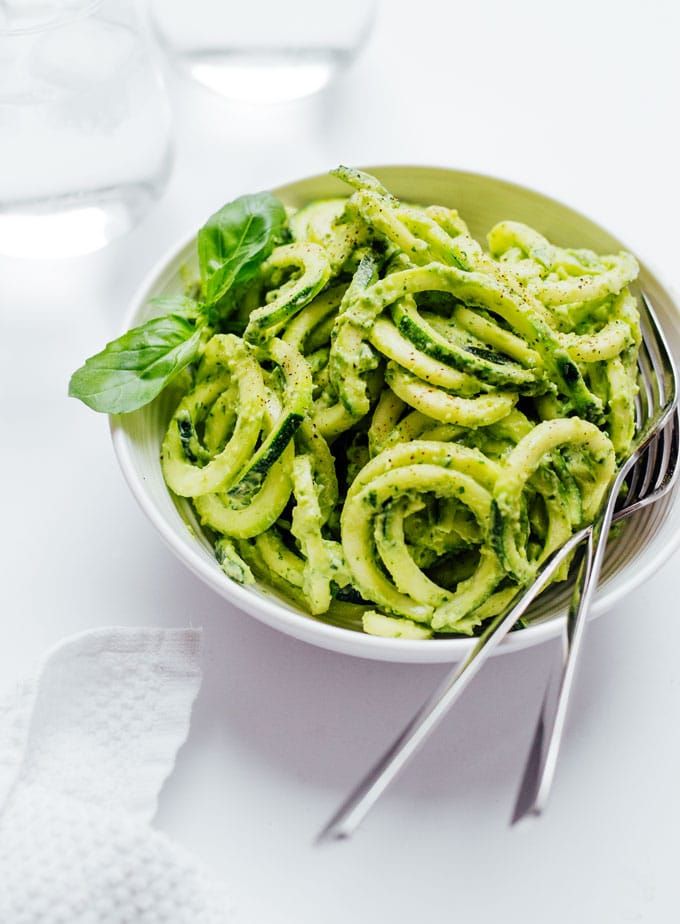 Un bol de nouilles avec sauce pesto et une fourchette sur une table.