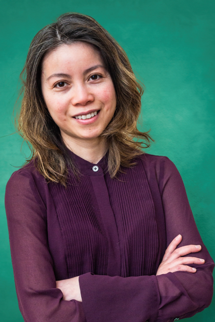 Dr. Claire Nguyen with crossed arms smiles in front of a green background, wearing a dark purple blouse.