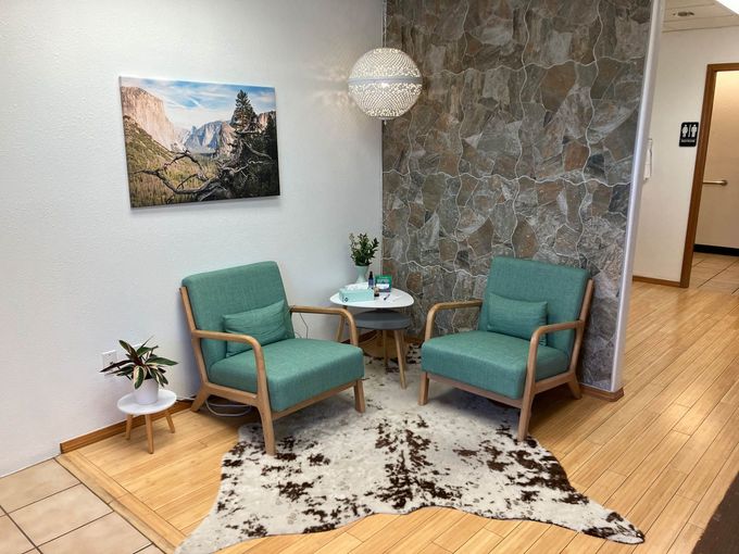 Two sage green armchairs face a small side table on a cowhide rug in an office lobby with stone wall and landscape art.