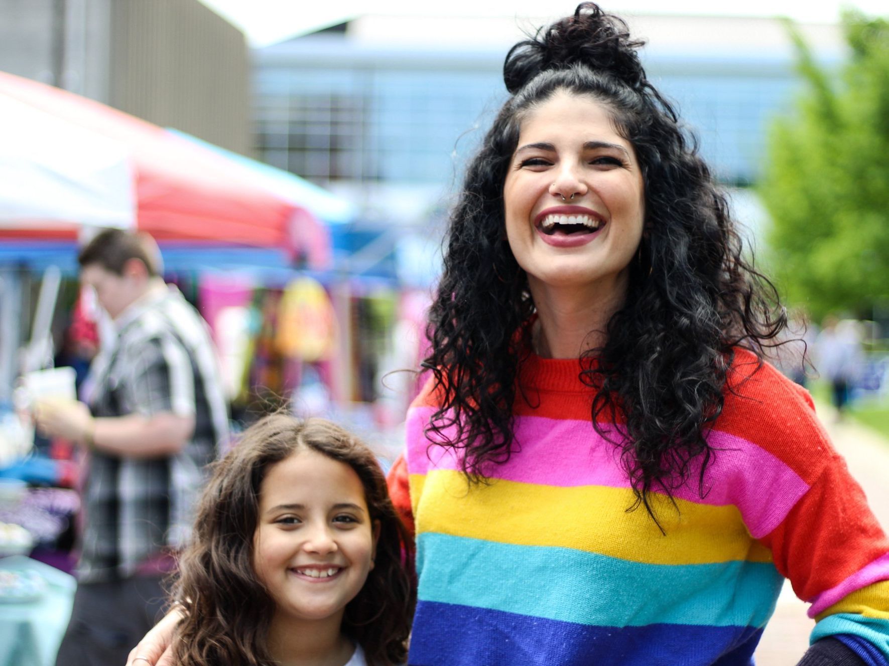 A woman in a rainbow sweater is standing next to a little girl.