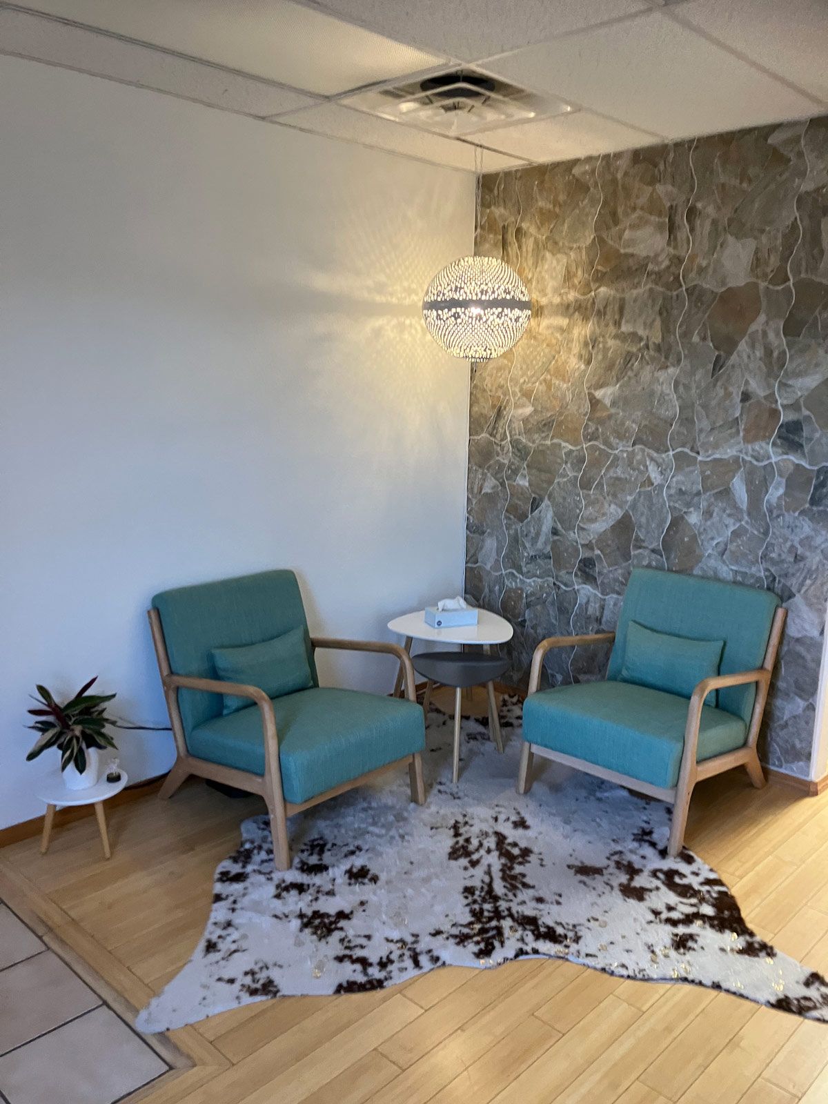 Two teal armchairs and small table on cowhide rug in cozy corner.