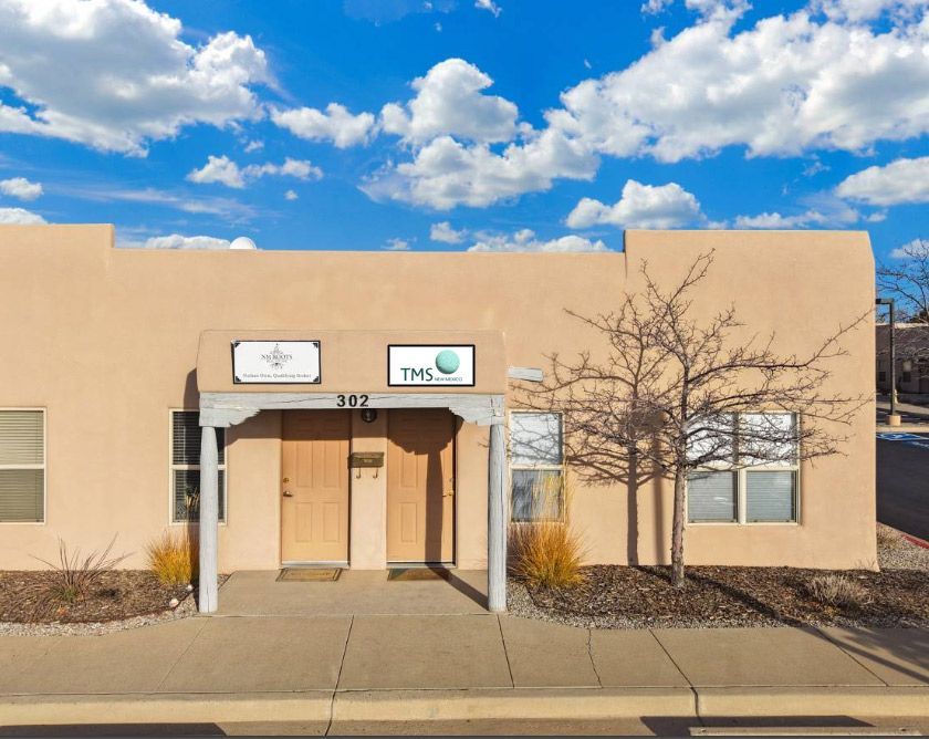 Exterior view of a stucco building with two doors and signs. The sky is blue with clouds.