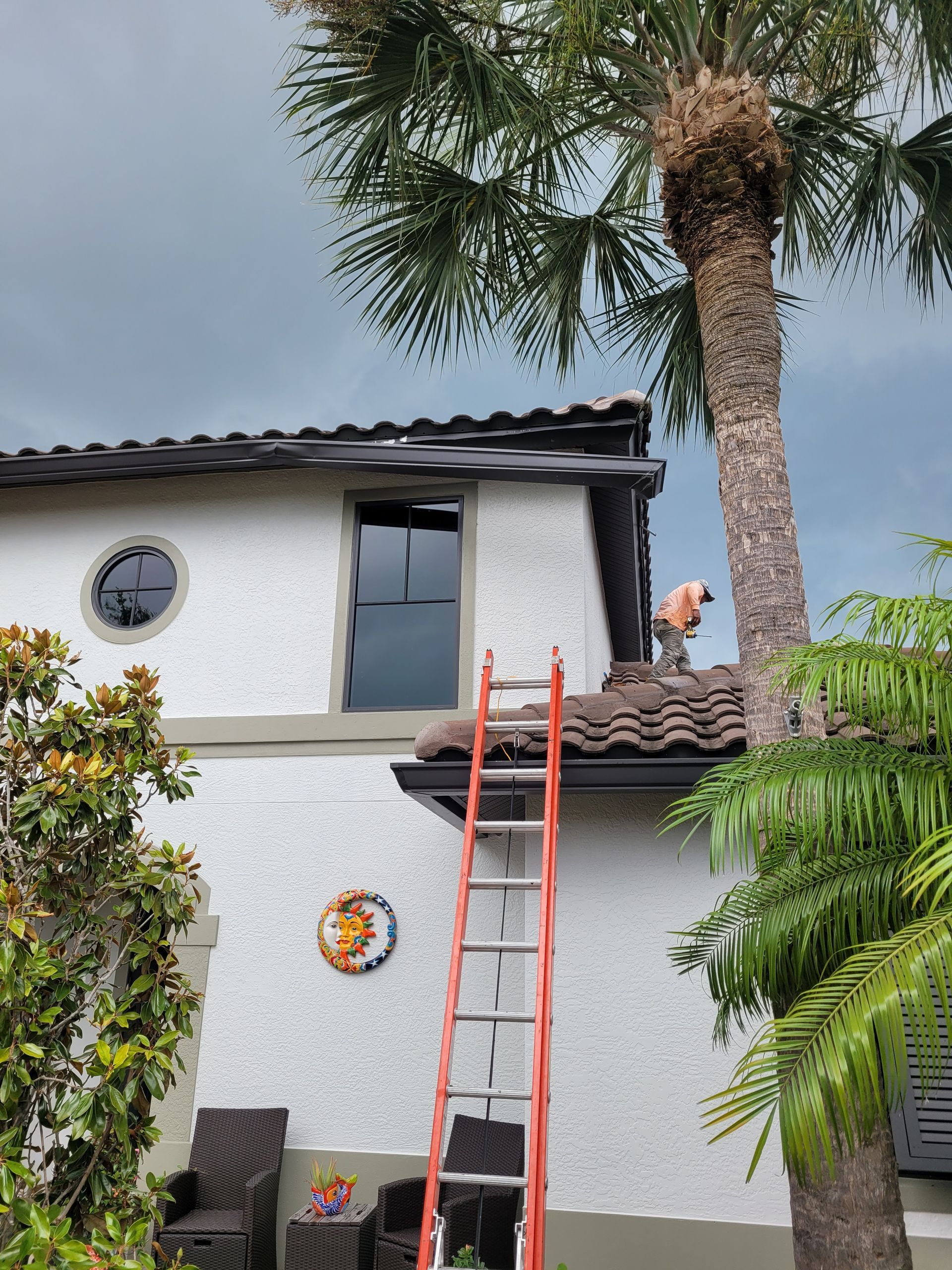 A man is standing on the roof of a house with a ladder.