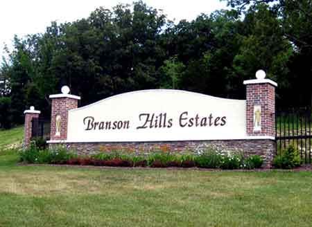 A sign for branson hills estates is sitting in the middle of a lush green field.