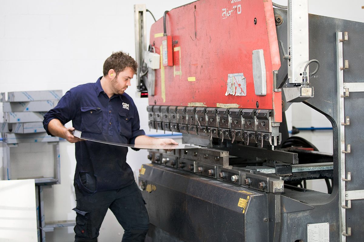 Man Bending Metal Sheet By Sheet Bending Machine — Sheet Metal Fabrication In Caloundra, Qld
