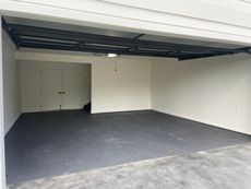 Empty garage with gray floor, white walls, and black ceiling beams.