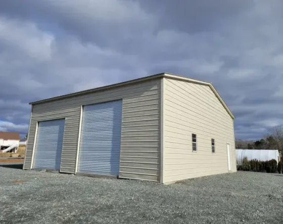 A metal garage with two garage doors is sitting on top of a gravel lot.