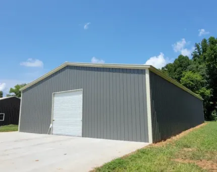 A large gray metal building with a white door is sitting in the middle of a grassy field.