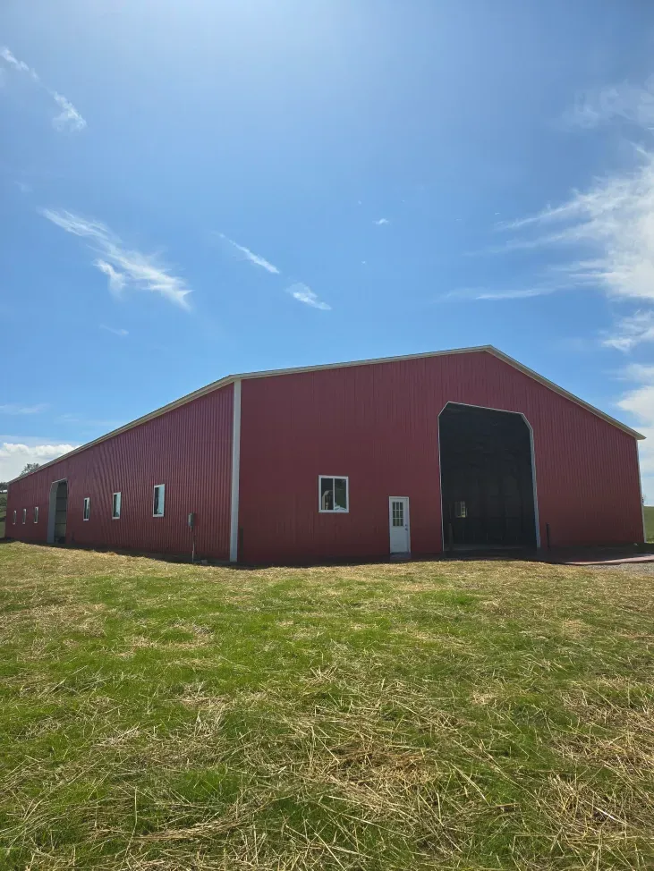 A large red barn is sitting in the middle of a grassy field.