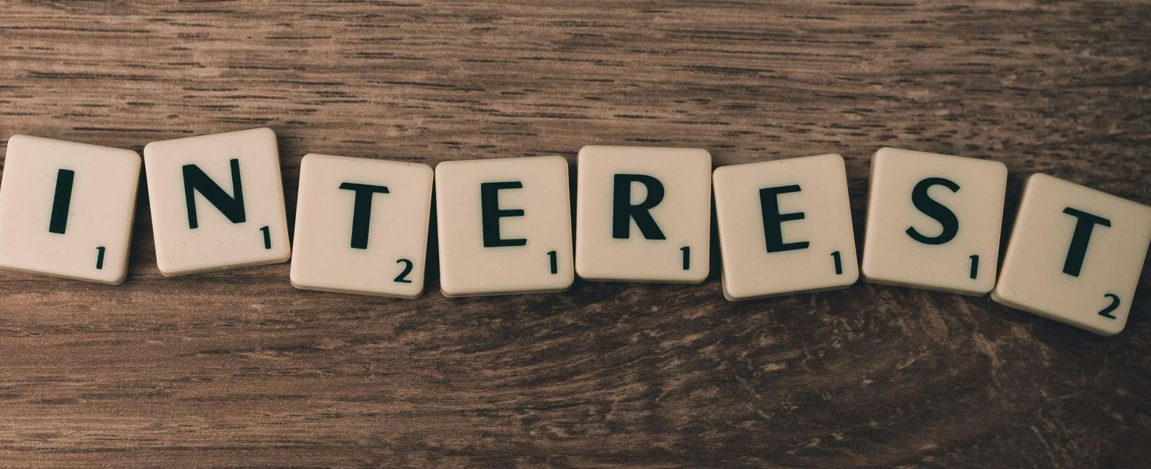 The word interest is written in scrabble tiles on a wooden table.