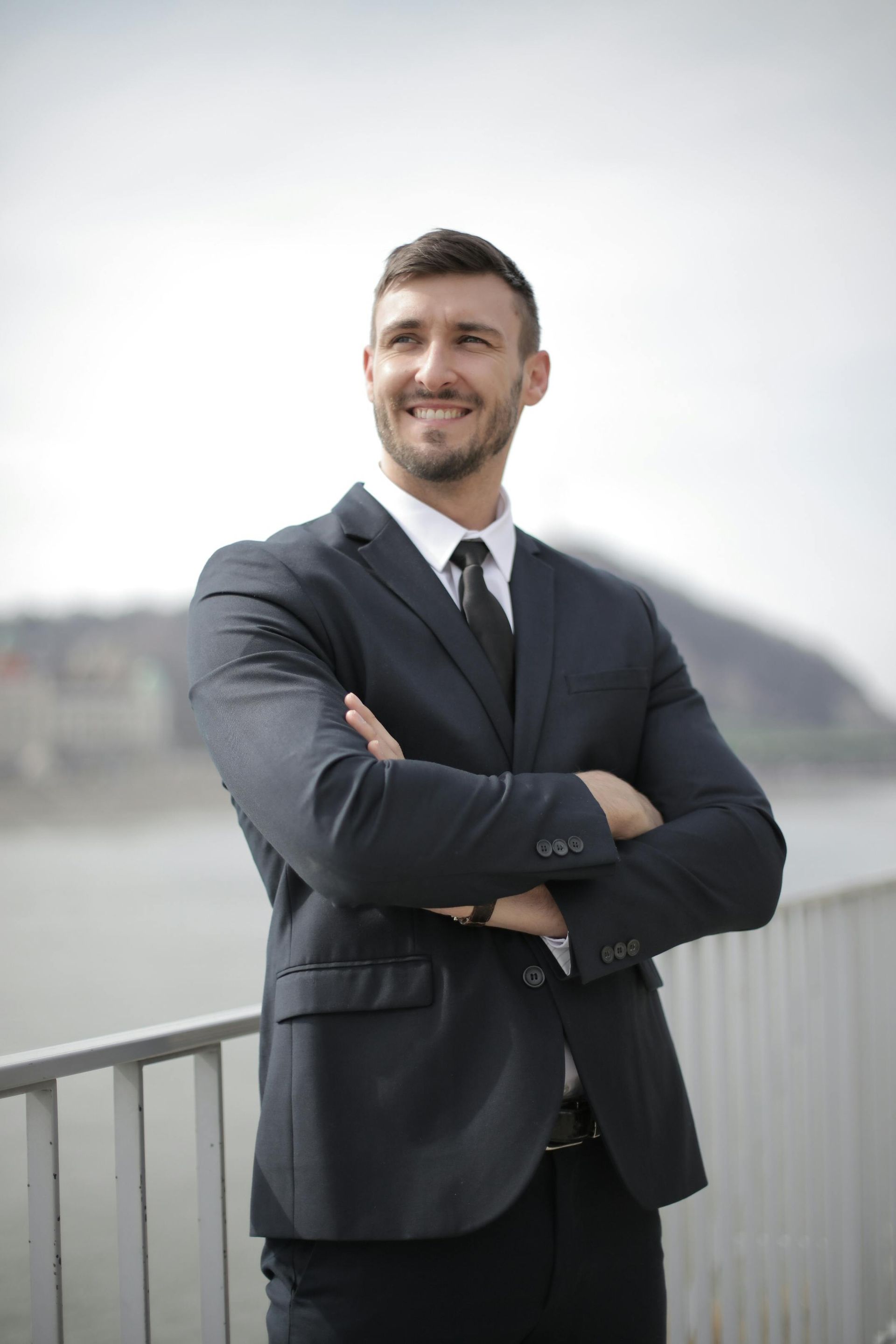A man in a suit and tie is standing on a bridge with his arms crossed.
