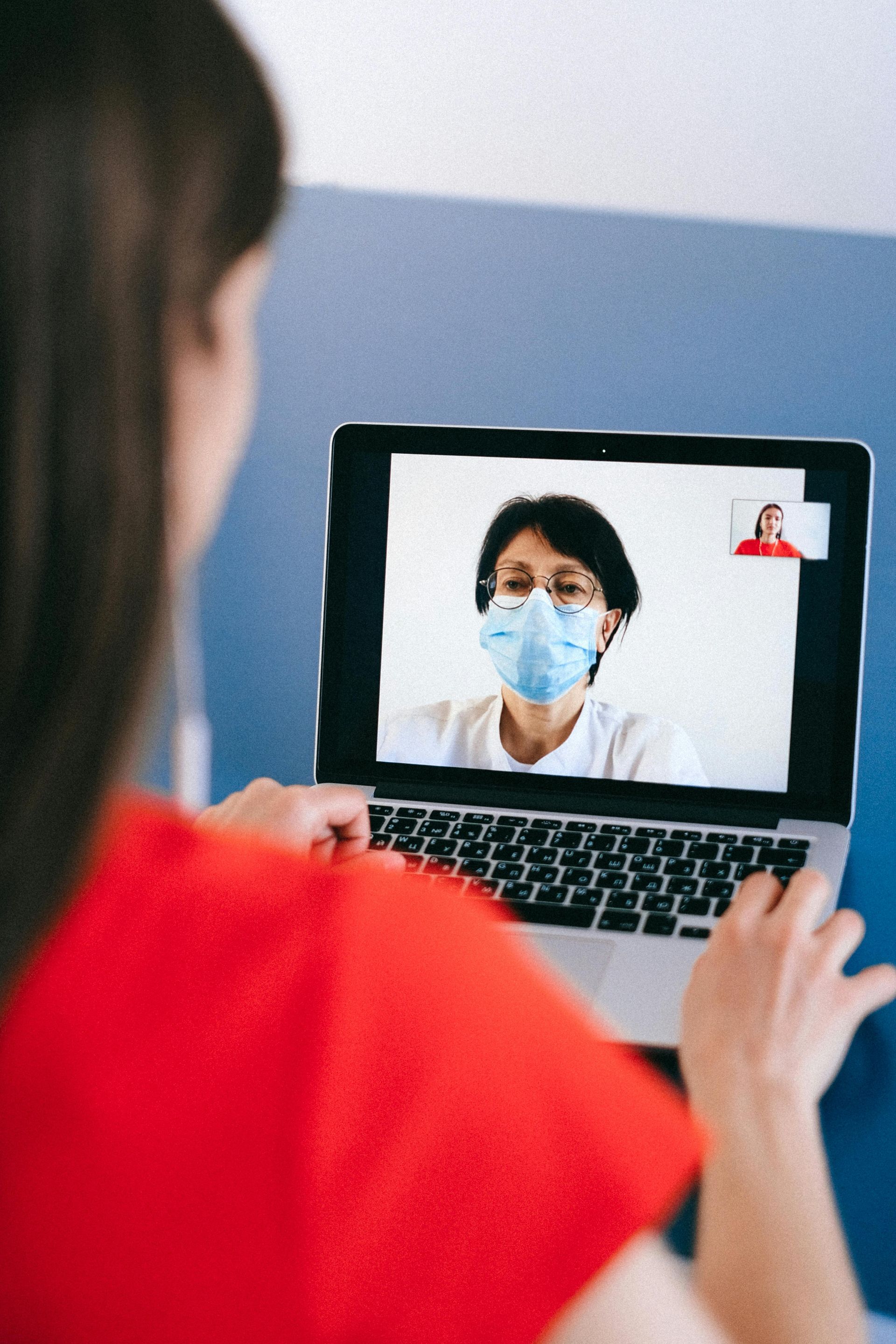 A woman wearing a mask is having a video call with a doctor on her laptop.