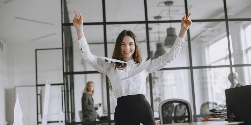 A woman is standing in an office with her arms in the air.