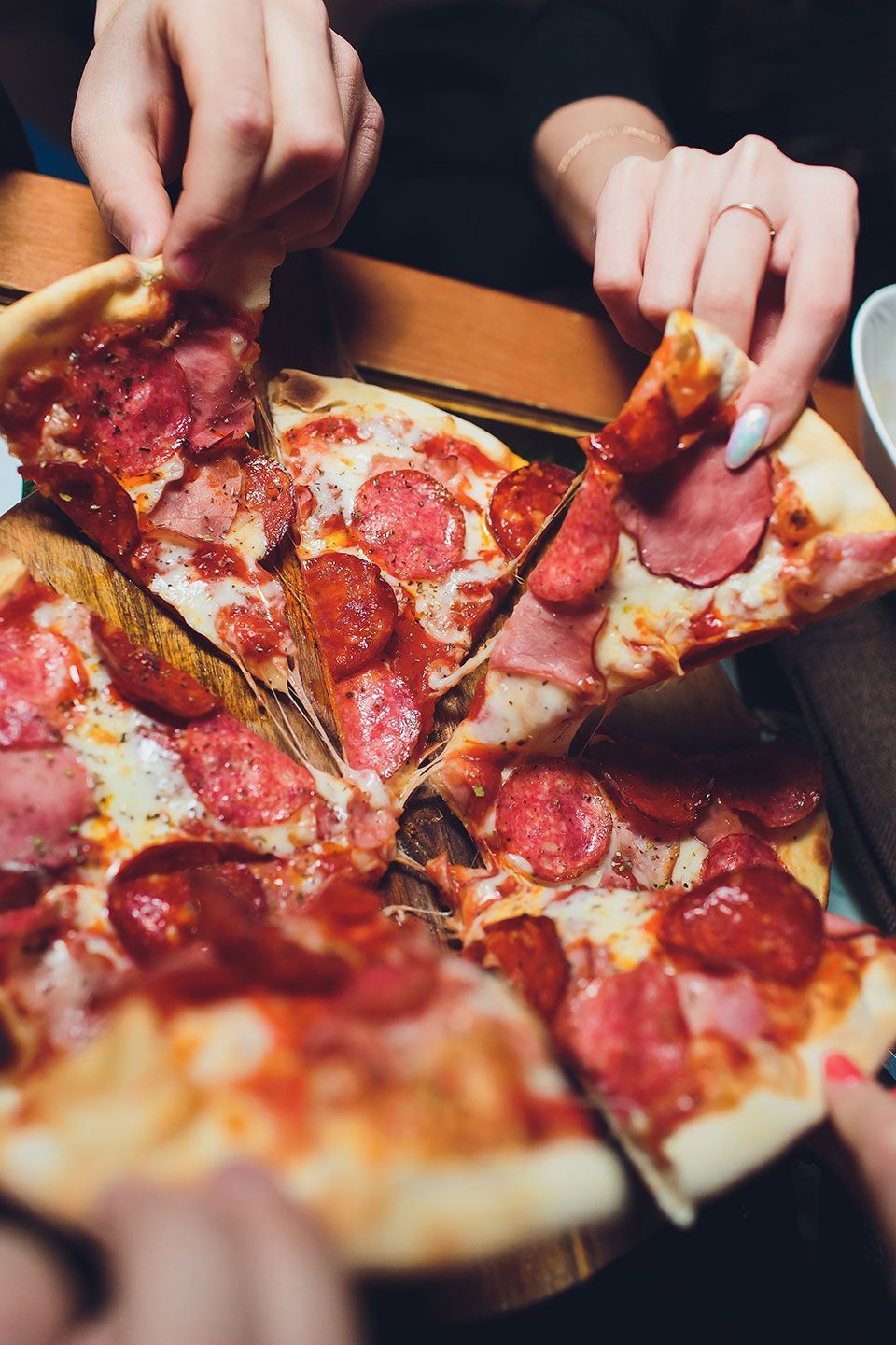 Hands grabbing pizza carbonara on rustic wooden table. Food photography concept