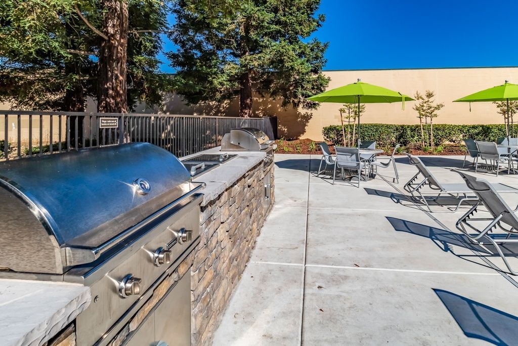 Outdoor community grilling area with stainless grill, stone counter, and green umbrellas.