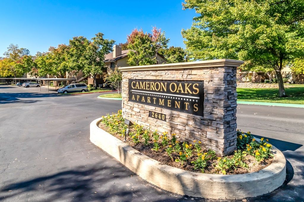 Stone sign reading CAMERON OAKS APARTMENTS at a landscaped entrance with a curved driveway.