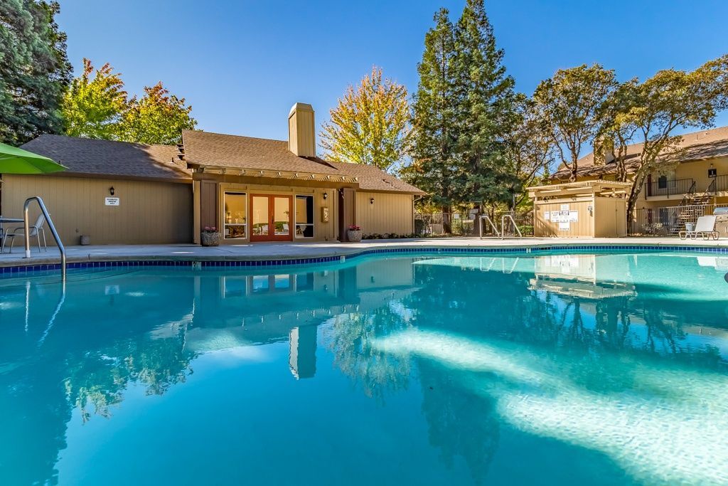 Outdoor swimming pool at a residential community with a clubhouse and surrounding trees.