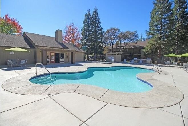 Outdoor community pool with curved shape, lounge chairs, and green umbrellas on a sunny day