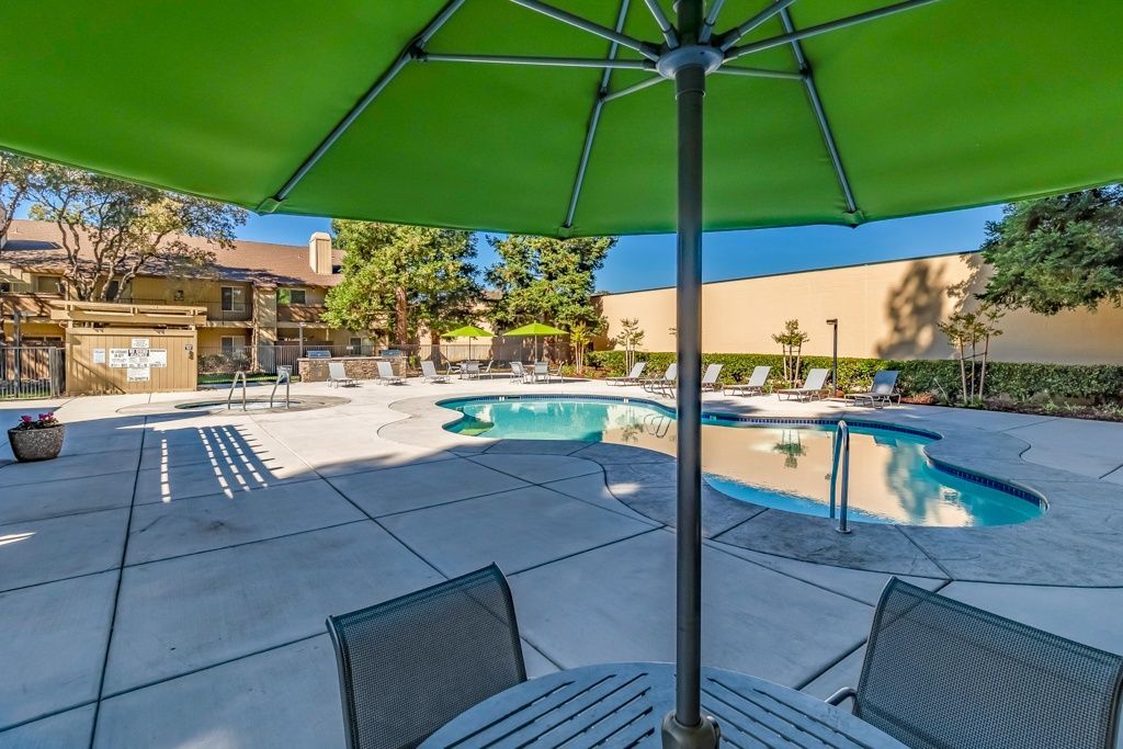 Outdoor community pool area with lounge chairs and a green shade umbrella overhead.