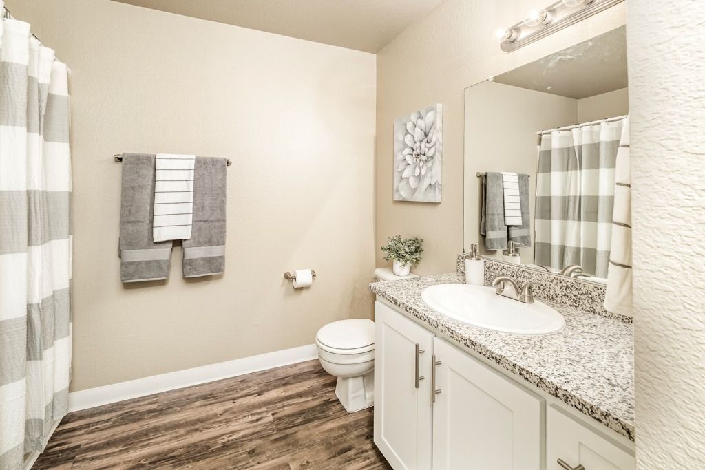 Bathroom with granite counter, white vanity, single sink, mirror, and striped shower curtain.