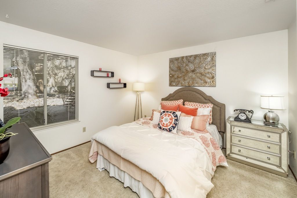 Bedroom in an apartment with a bed, nightstands, lamp, and window blinds.