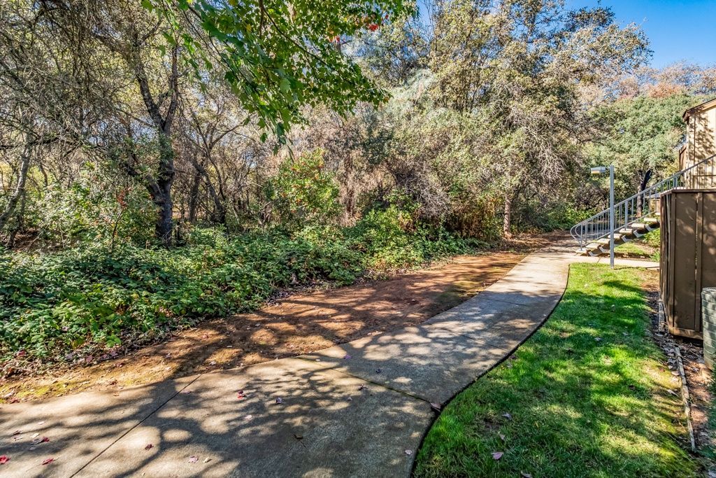 Curved concrete walkway through trees with an exterior stairway on the right.