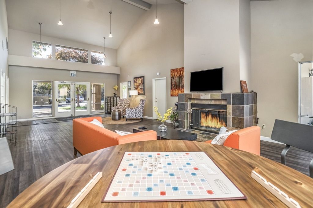 Lobby-style residents lounge with orange sofas, a stone fireplace, a round table, and a wall-mounted TV.