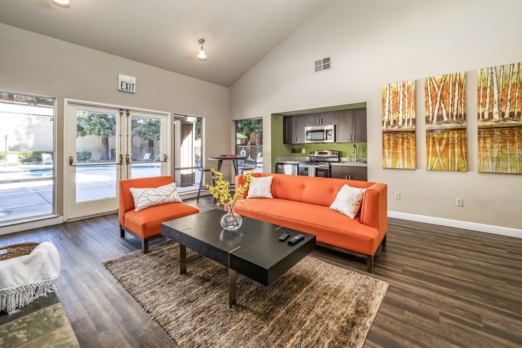 Indoor community lounge with an orange sofa, coffee table, rug, and kitchenette; doors to pool.