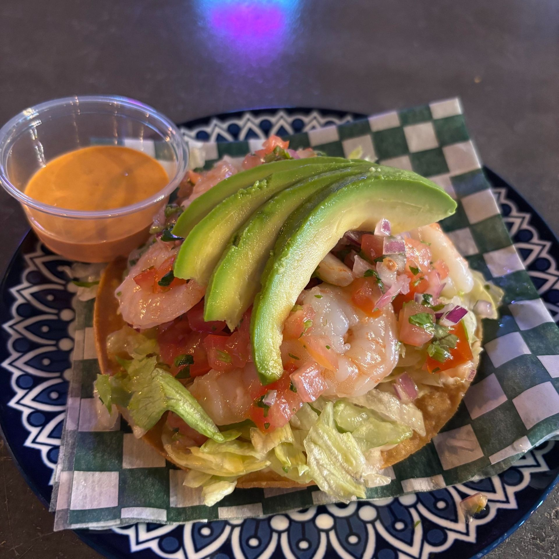 Shrimp tostada with avocado, salsa, and sauce on a decorative plate.