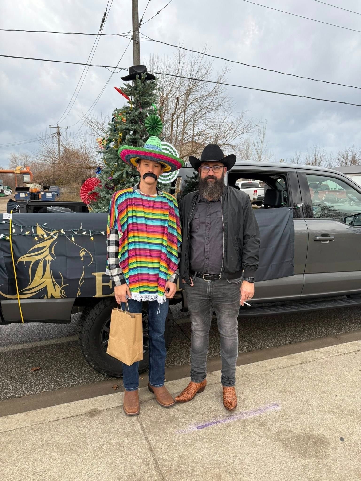 Two people posing by a decorated truck. One in a sombrero and poncho, the other in a cowboy hat and boots.