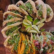 Tacos on wooden board with lime wedges. Corn and flour tortillas filled with meat, cilantro, and onions.