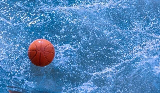 A basketball is floating in the water of a swimming pool.