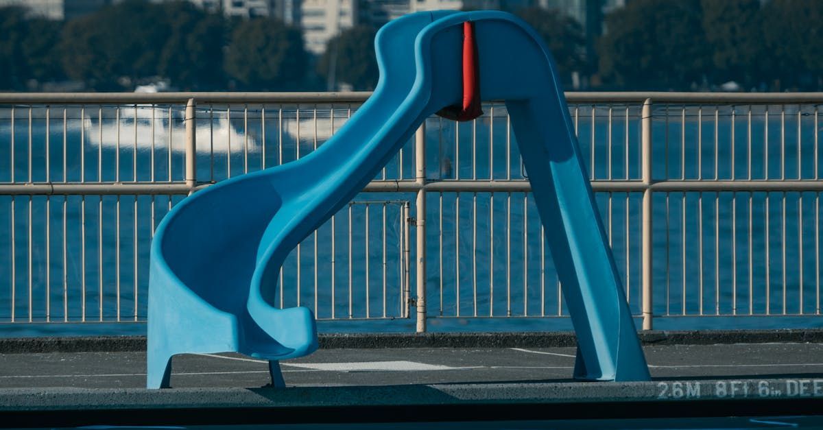 A blue slide is sitting next to a fence next to a pool.