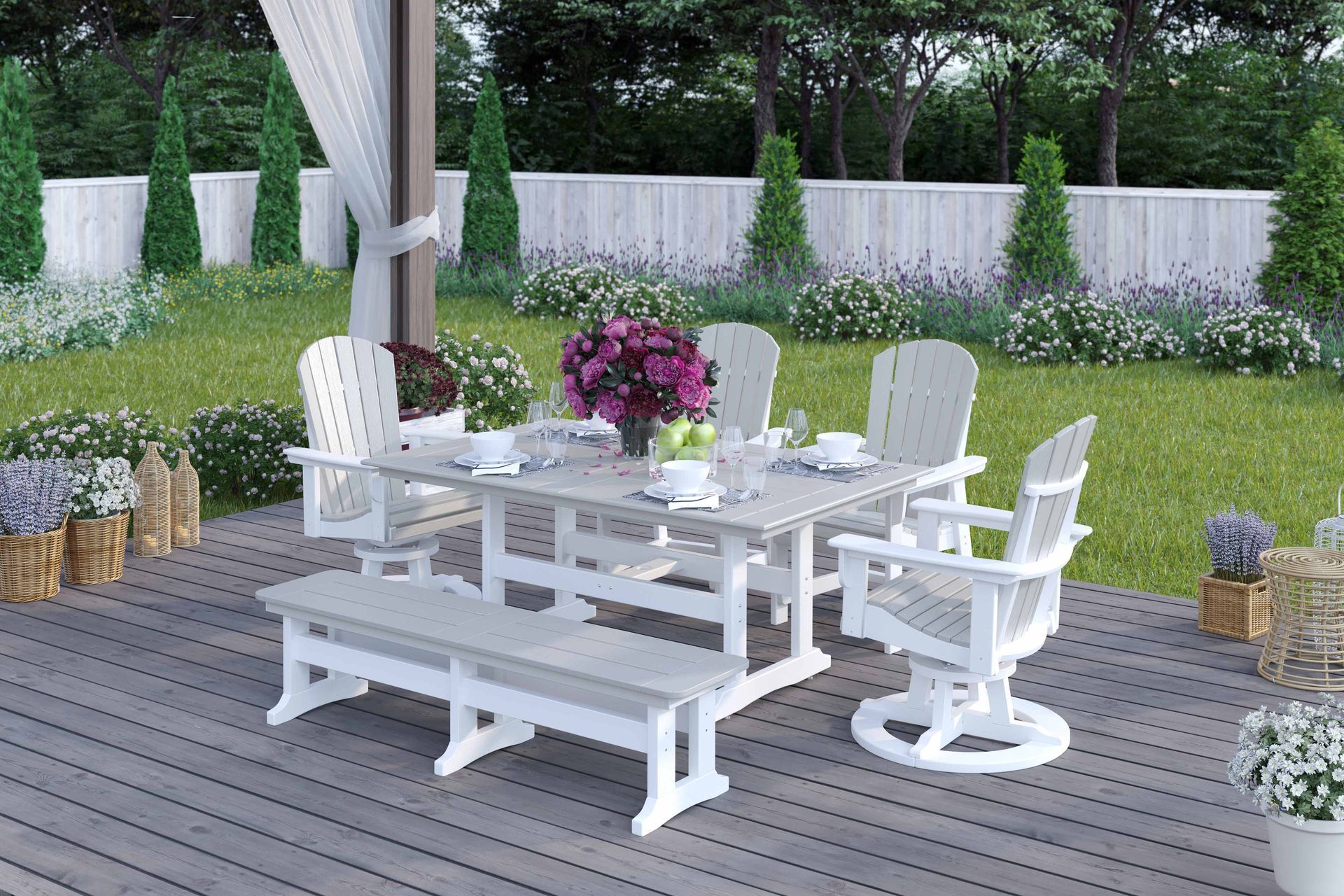 Outdoor dining set on a deck: gray table, white chairs, bench; flowers in vases, green lawn, white fence.