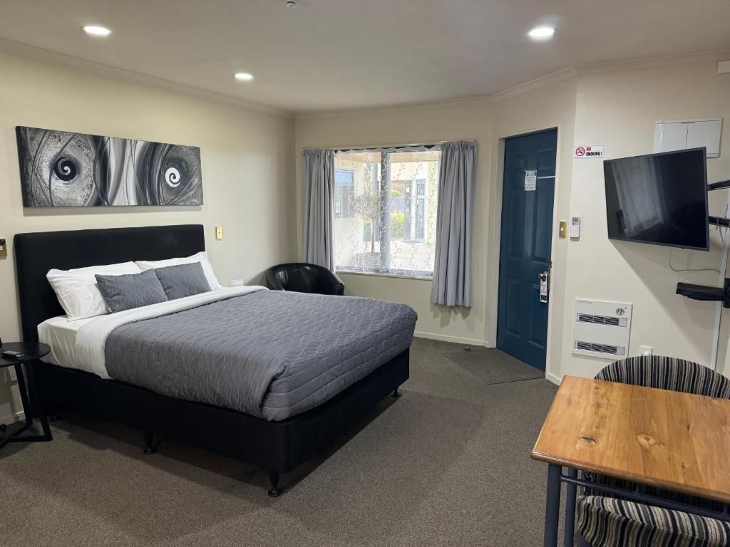 A hotel room with a king size bed , table , chair and television.