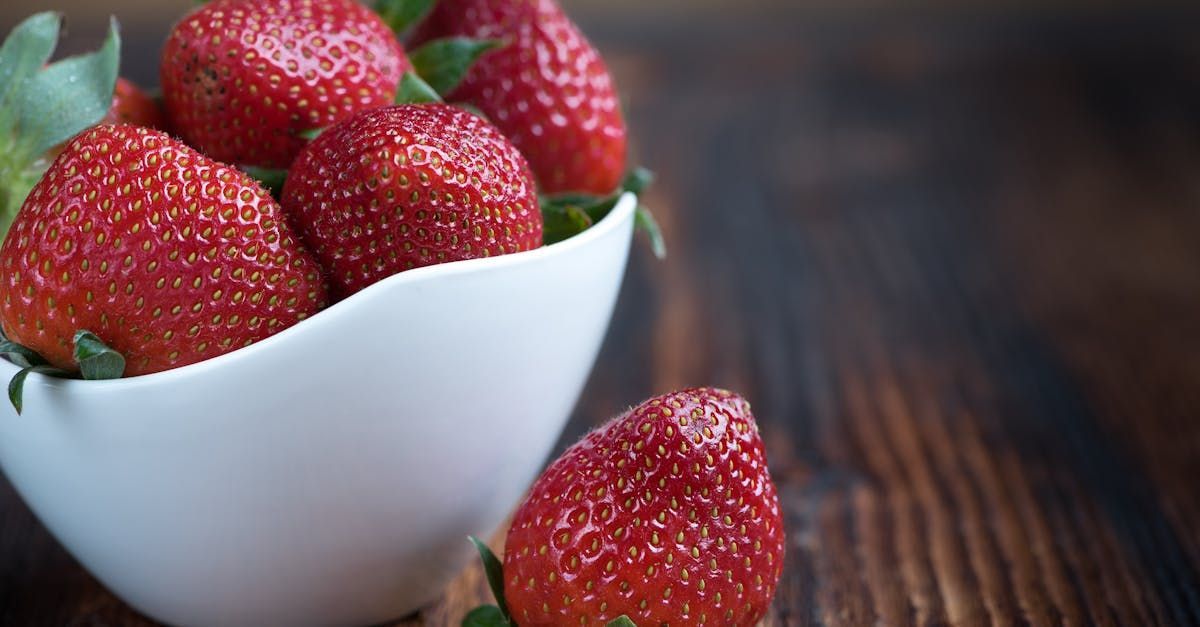 Strawberries are in a white bowl on a wooden table.