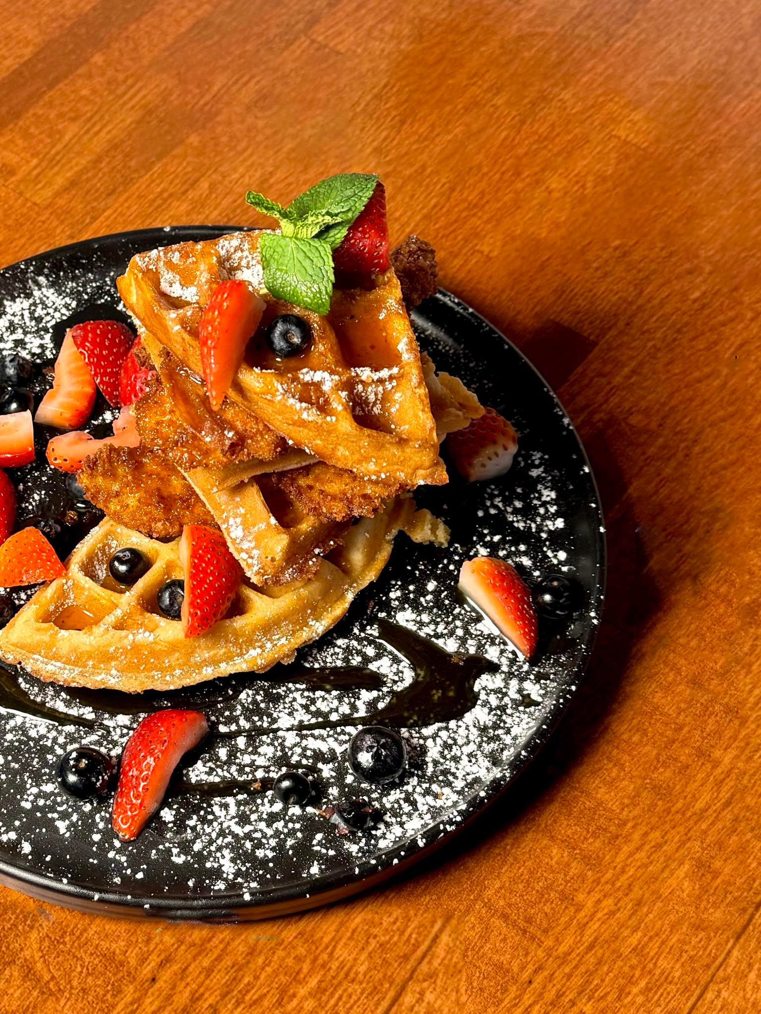 A plate of waffles with strawberries and blueberries on a wooden table.